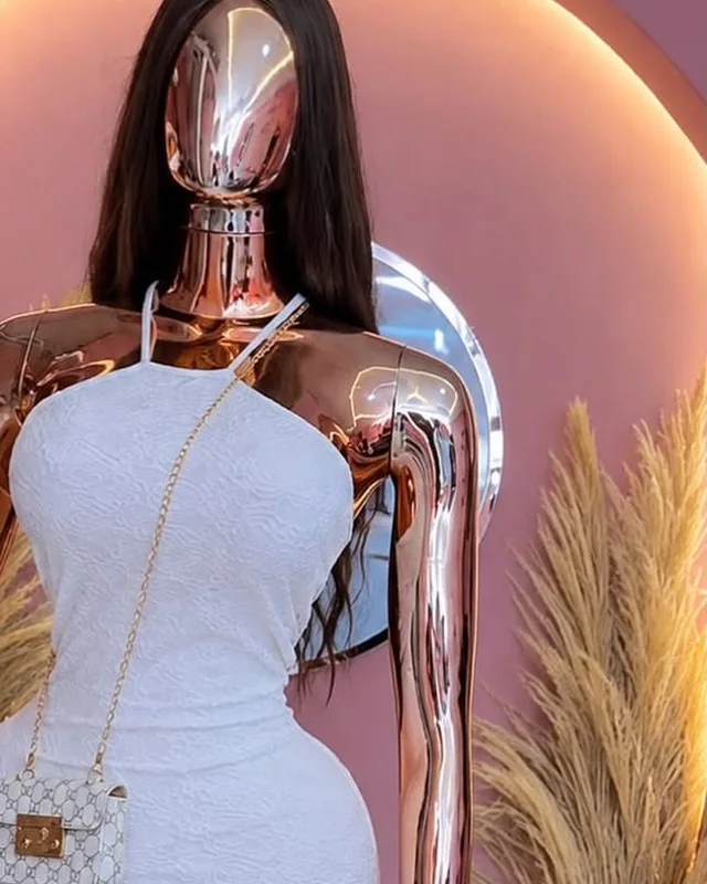 Vestido blanco de encaje en un maniquí rosa dorado frente a un arco de luz